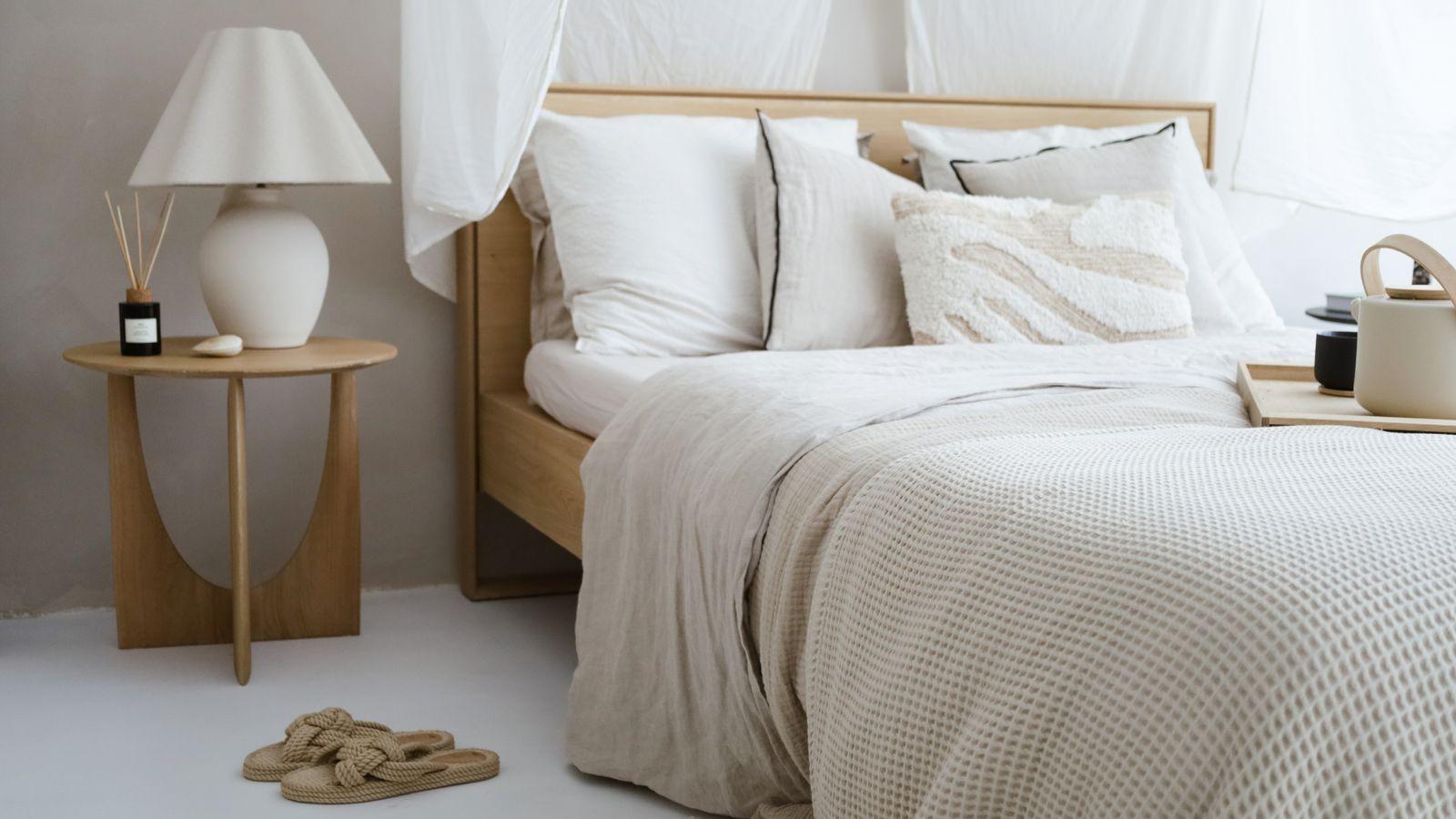 Cama con ropa de cama de lino en tonos neutros y mesilla de madera
