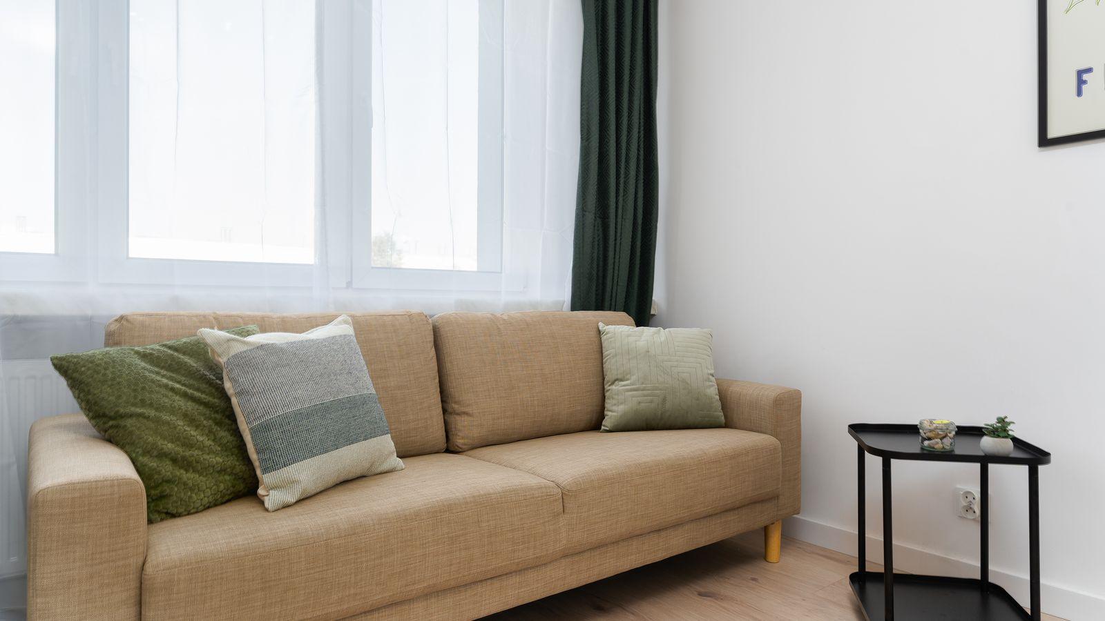 Salón en tonos neutros con sofá beige, cojines verdes y cortinas de lino
