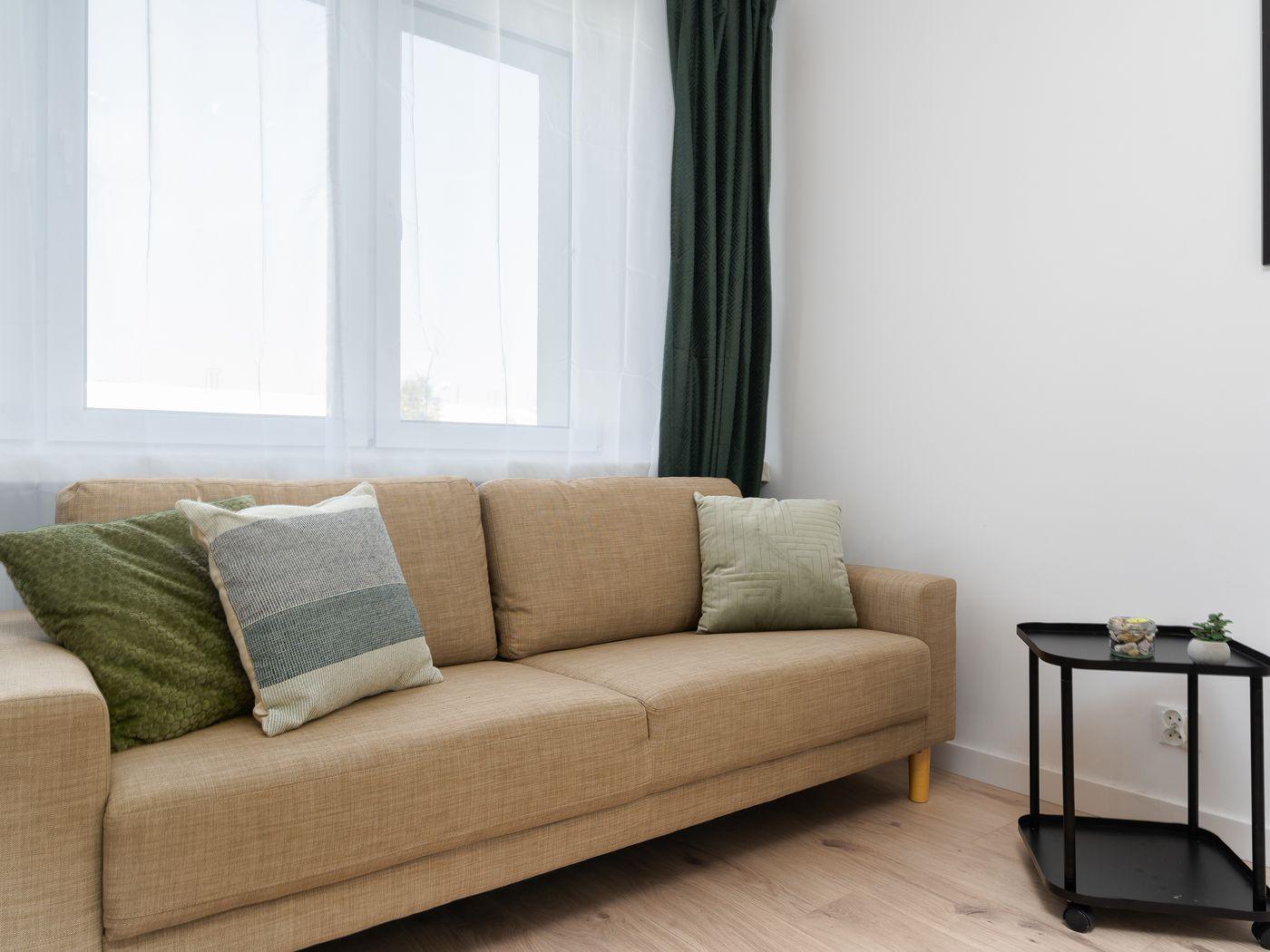 Salón con sofá beige y cojines verdes junto a una ventana